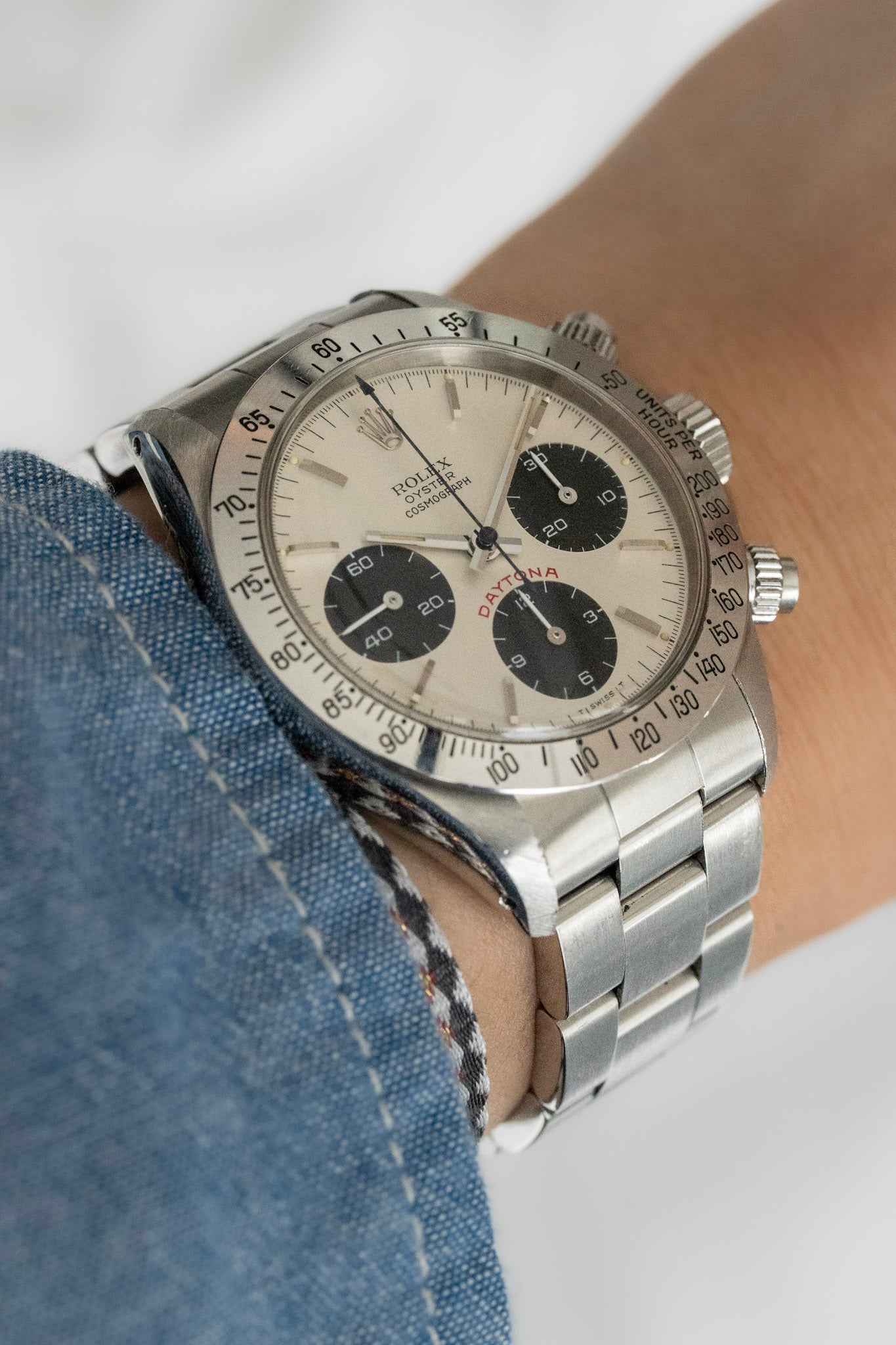 A close-up of a wrist wearing a stainless steel Cosmograph Daytona 6265 with a cream dial.